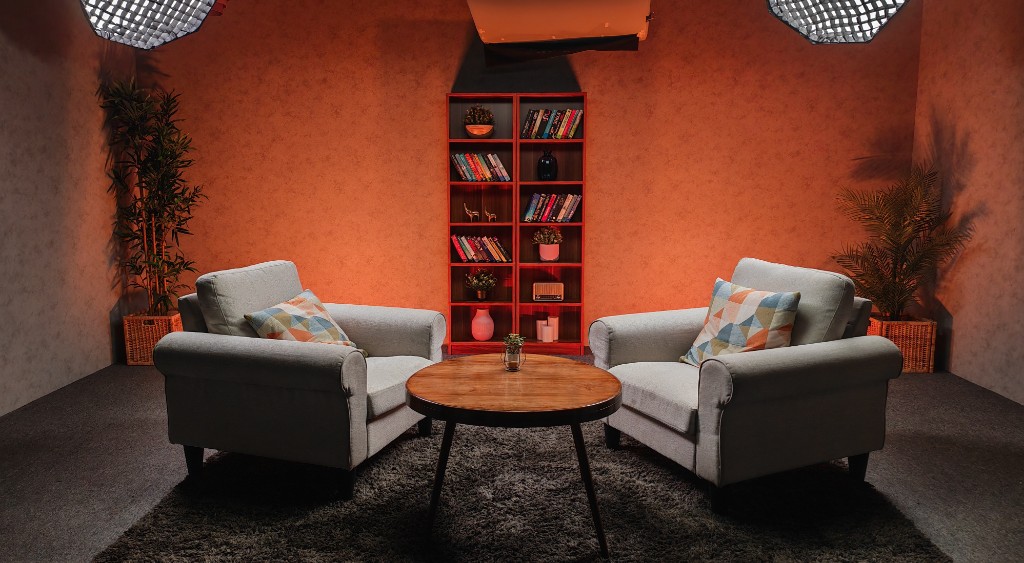Custom brand podcast studio with grey armchairs, terracotta wall, bookshelf backdrop, and studio lighting at Winterfox Studios